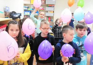 Dwoje uczniów trzyma w rękach kolorowe balony z namalowanymi na nich liczbami.
